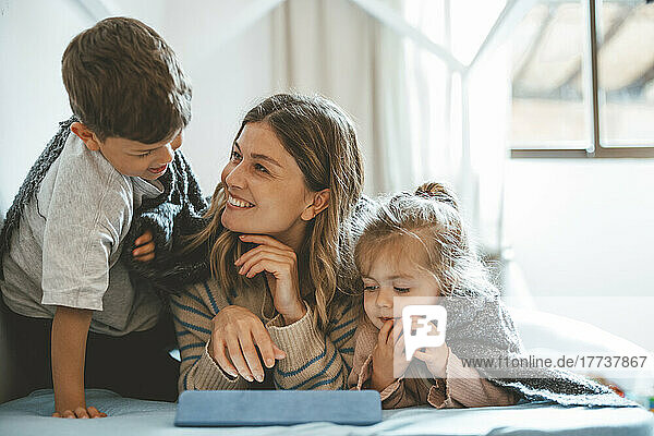 Smiling mother with son and daughter on bed at home