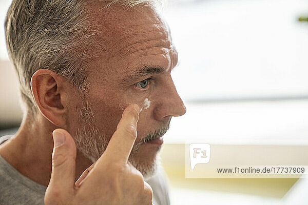 Man applying cream on face in bathroom