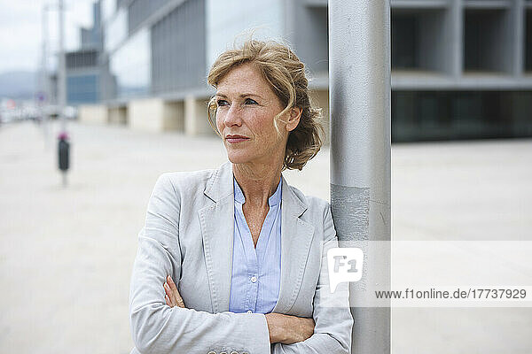 Businesswoman standing with arms crossed leaning on pole