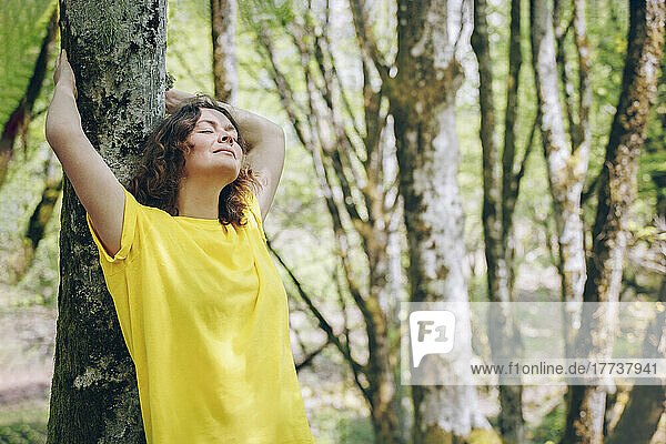 Carefree woman leaning on tree trunk in forest