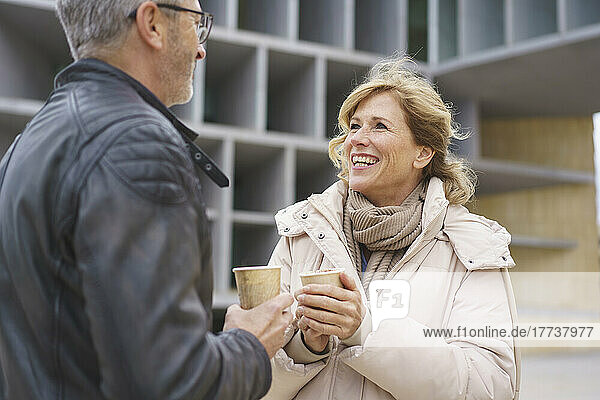 Happy woman and man holding disposable coffee cup standing in front of building