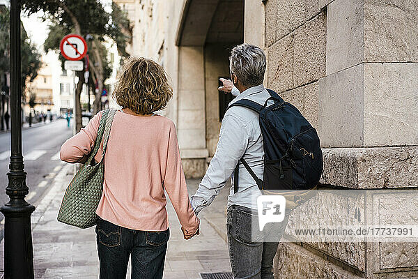 Älteres Paar hält sich an den Händen und geht im Urlaub auf dem Fußweg