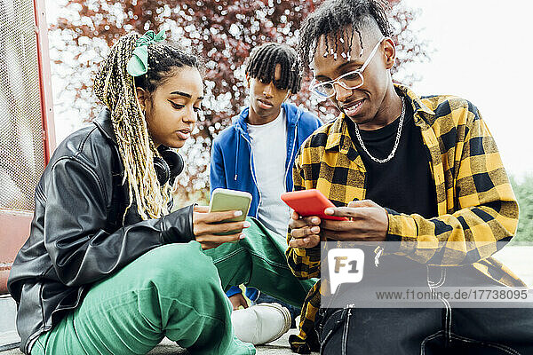 Young man and woman using smart phone sitting in front of friend