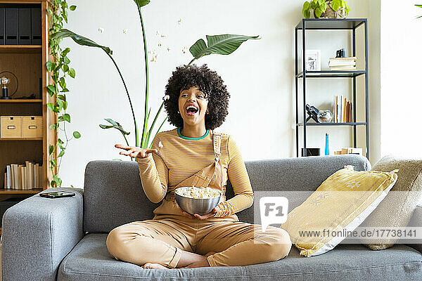 Playful woman throwing popcorn sitting on sofa at home