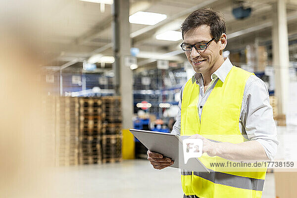 Smiling worker wearing eyeglasses using tablet PC in warehouse