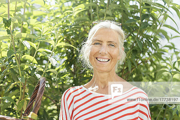 Happy mature woman in front of plants on sunny day