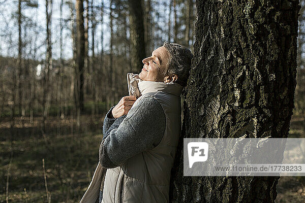 Woman with closed eyes leaning against tree trunk