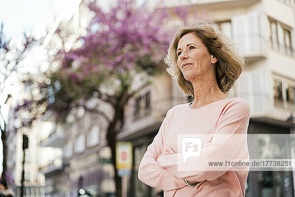 Thoughtful mature woman with arms crossed in city