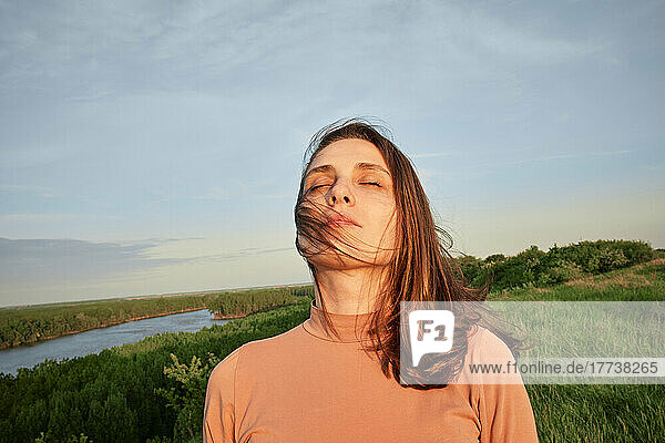 Young woman with eyes closed in sunlight at agricultural field