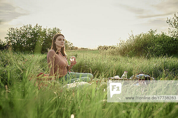 Thoughtful woman having infused water in field on weekend