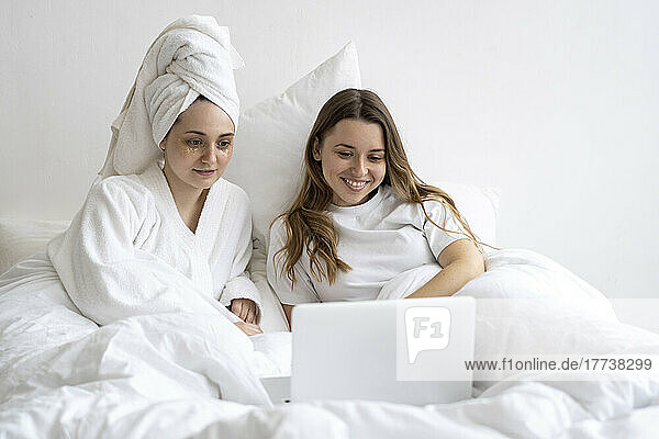 Fröhliche Freunde liegen auf dem Bett und schauen auf den Laptop