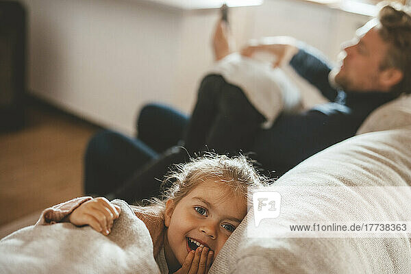Smiling cute girl sitting by father on sofa