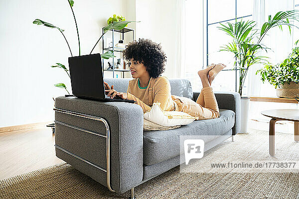 Young woman using laptop lying on sofa at home