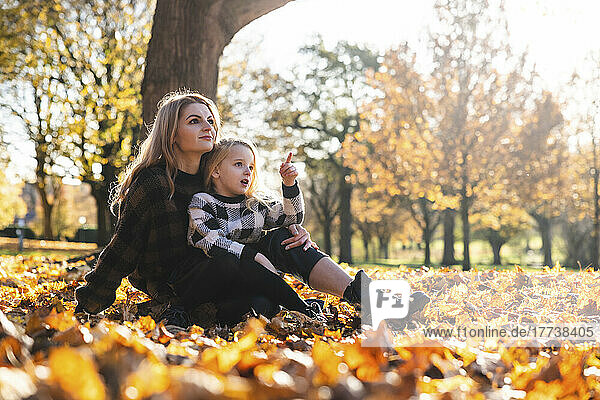 Daughter gesturing sitting with mother at autumn park