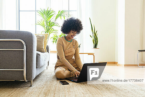 Glückliche Frau  die zu Hause auf dem Teppich sitzt und einen Laptop benutzt