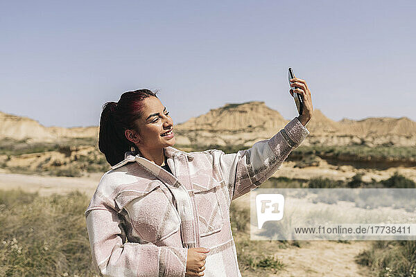 Smiling woman taking selfie through smart phone on sunny day
