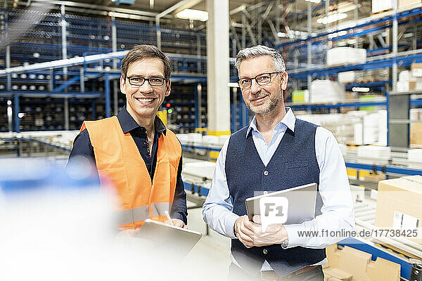 Happy worker standing by manager holding tablet PC in warehouse