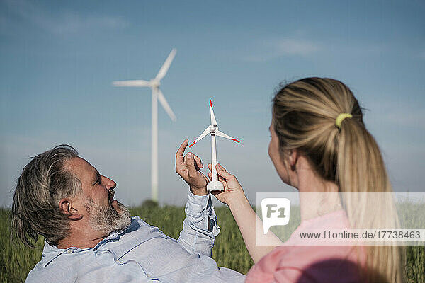 Woman holding wind turbine model sitting with man in field on sunny day