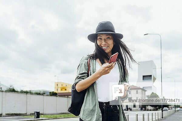 Happy young woman wearing hat standing with smart phone