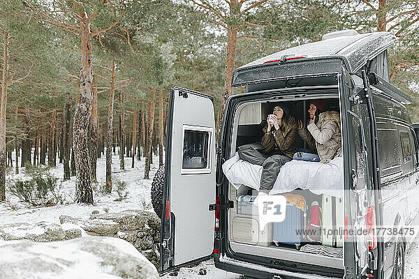 Woman drinking coffee sitting with friend in campervan