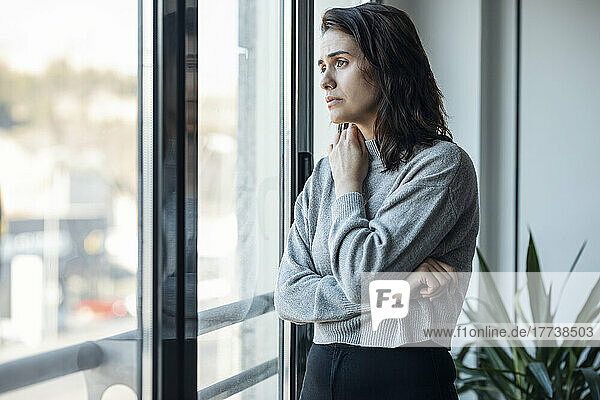 Thoughtful sad woman looking through window at home