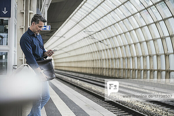 Businessman surfing net through smart phone standing at railroad station