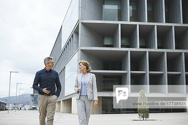 Businessman discussing with businesswoman walking in front of office building