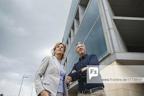 Businessman with arms crossed standing by businesswoman in front of office building