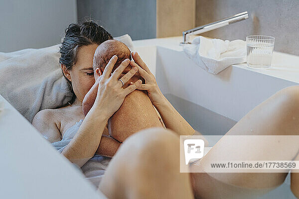 Naked mother playing with son in bathtub at home