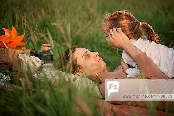 Mother talking with daughter lying on grass