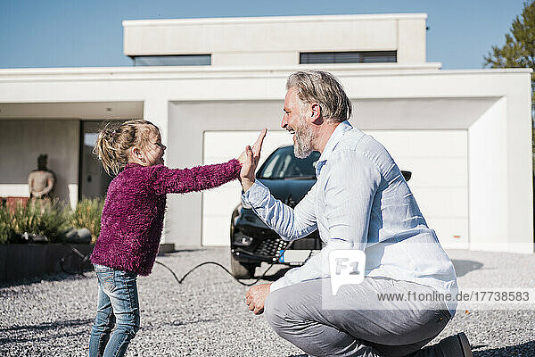 Happy girl giving high five to father in front of car on sunny day