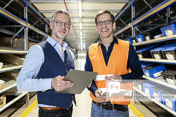 Smiling manager and worker standing together in aisle at warehouse