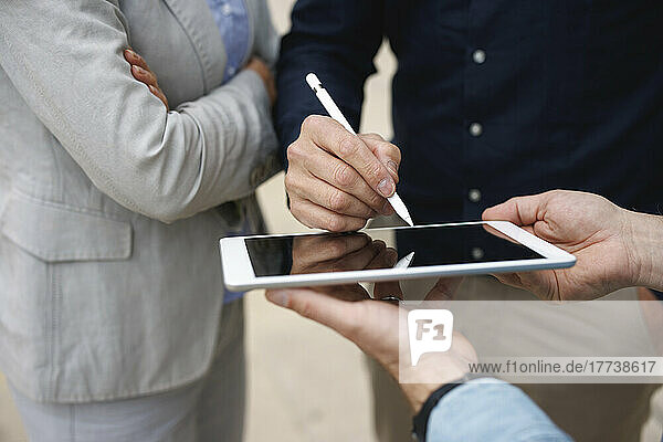 Hand of businessman signing on tablet PC standing by colleagues