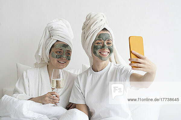 Happy friends wearing facial masks taking selfie through mobile phone