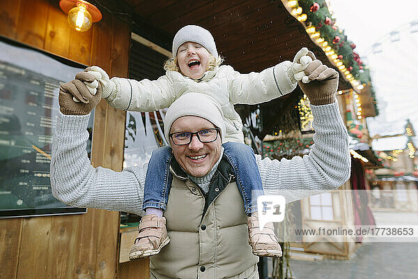 Smiling father carrying daughter on shoulders at Christmas market
