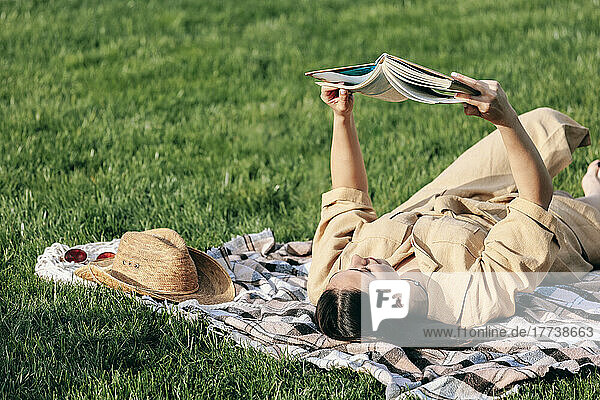 Young woman reading book lying on picnic blanket at park