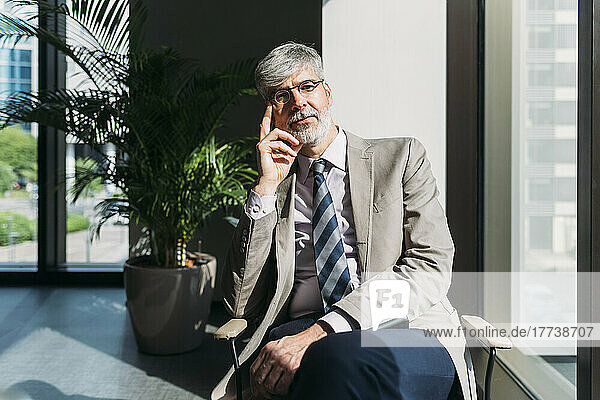 Mature businessman wearing eyeglasses sitting on chair by window at office