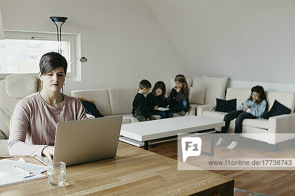 Mother working on laptop with children sitting in living room at home