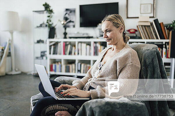 Frau sitzt zu Hause im Sessel und benutzt Laptop