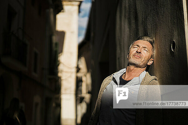 Mature man with eyes closed leaning on wall at sunny day
