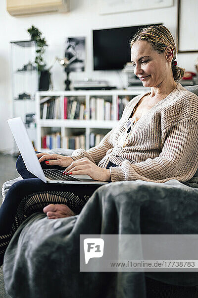 Smiling woman using laptop sitting on armchair at home