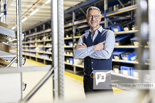 Happy manager wearing eyeglasses standing with arms crossed in warehouse