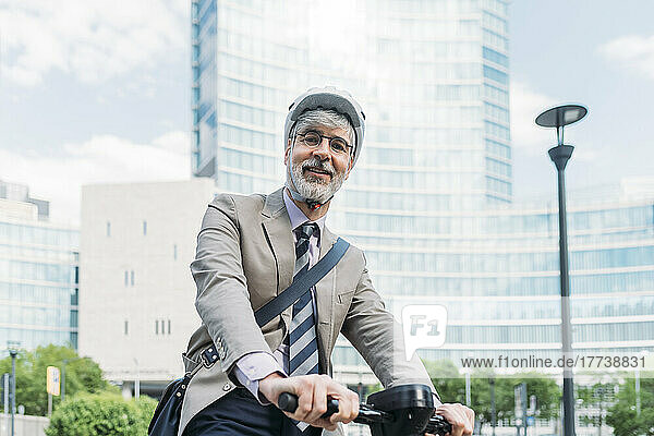 Happy businessman with electric push scooter in front of office buildings
