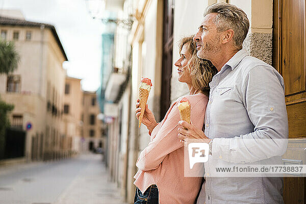 Thoughtful mature couple with ice cream standing in alley