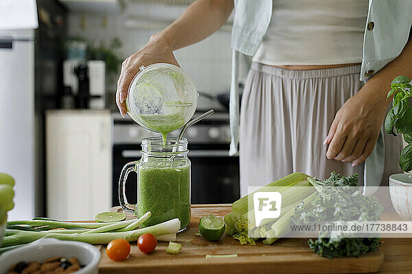 Hand of woman pouring smoothie in mason jar from juicer at home