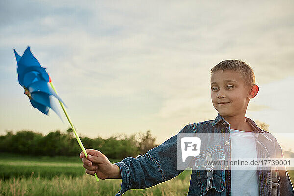 Boy playing with blue pinwheel toy in agricultural field