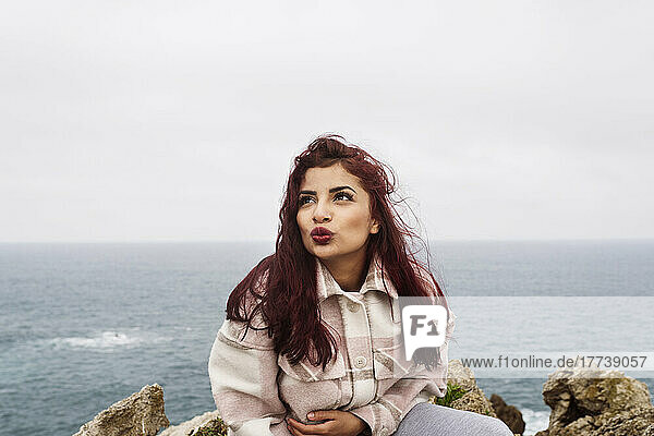 Woman with red hair puckering lips sitting on rock