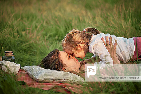 Mother and daughter rubbing noses lying on grass at picnic