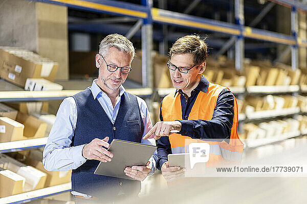 Worker pointing on tablet PC discussing with manager in warehouse