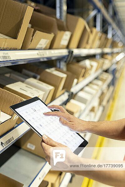 Hands of worker analyzing list on tablet PC by rack in warehouse